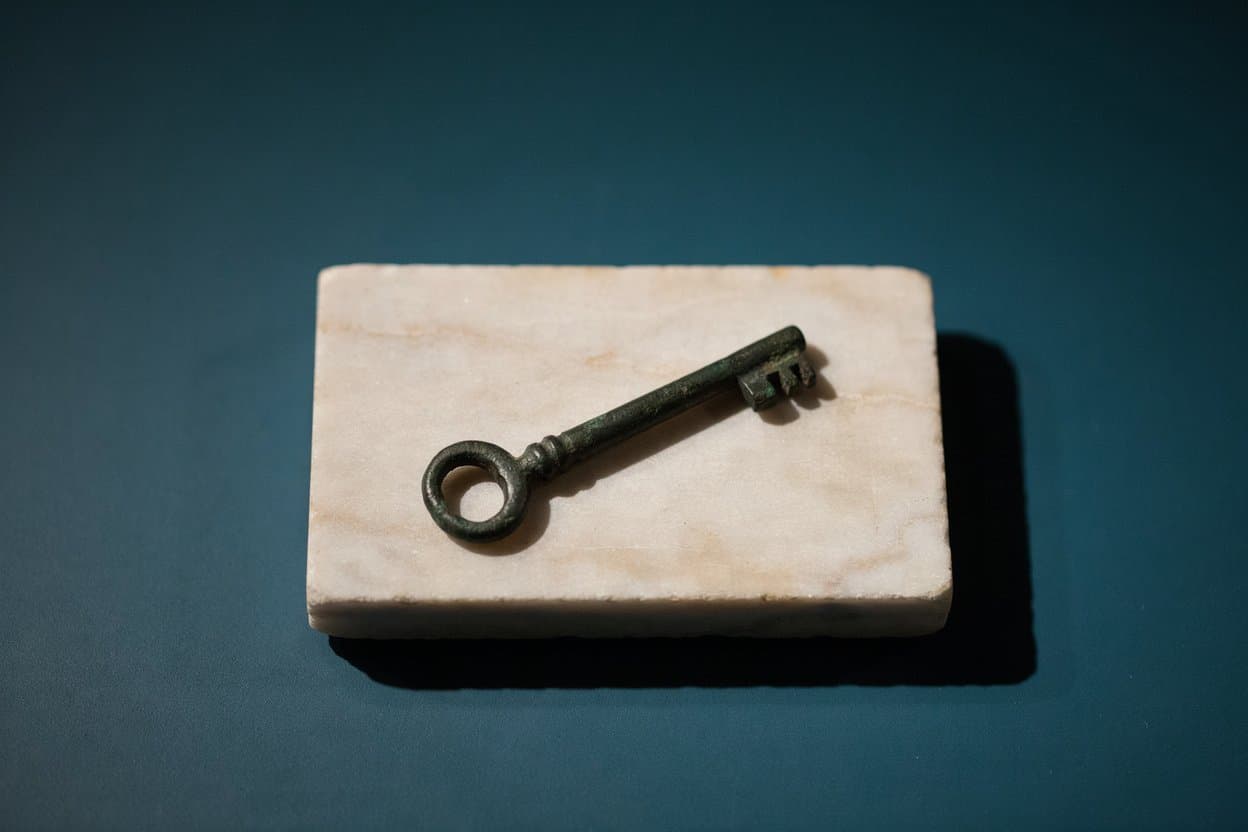 A Roman bronze key with a toothed bit, lying on a veined marble slab.